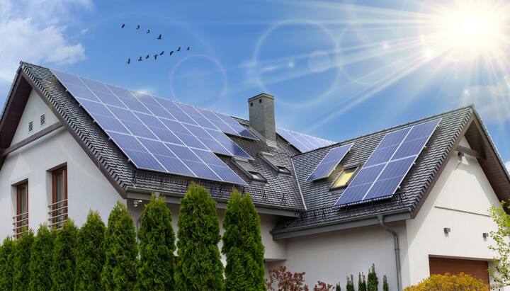 A close-up view of a residential rooftop solar panel installation in Cumming, GA. The solar panels are arranged in a neat pattern and angled towards the sun to capture the maximum amount of energy. The roof of the house is visible in the background, with clear blue skies and a few clouds.